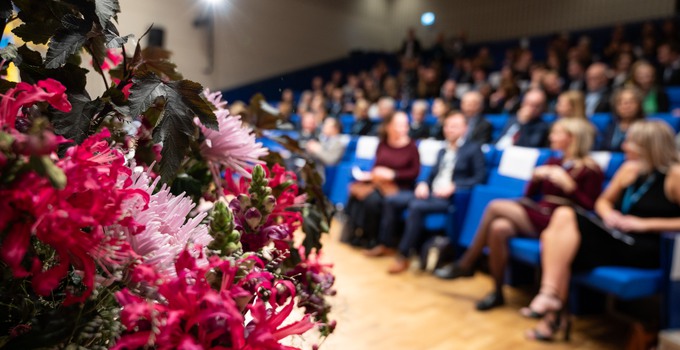 föreläsningssal med festklädda personer, blommor i förgrunden