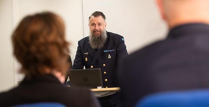 Person in a military uniform in a rostrum speaking to a small audience. 