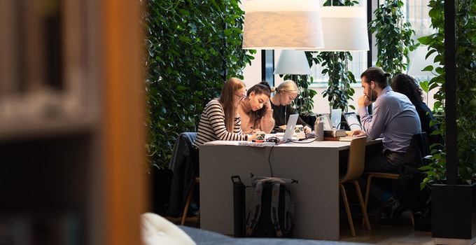 Studenter som sitter vid ett bord och läser framför ett fönster. 