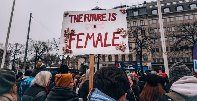 Demonstration där kvinnor håller upp plakat med texten the future is female. 