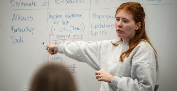 Emelie Moregård står upp och pratar framför sina kurskamrater och pekar på en whiteboardtavla.