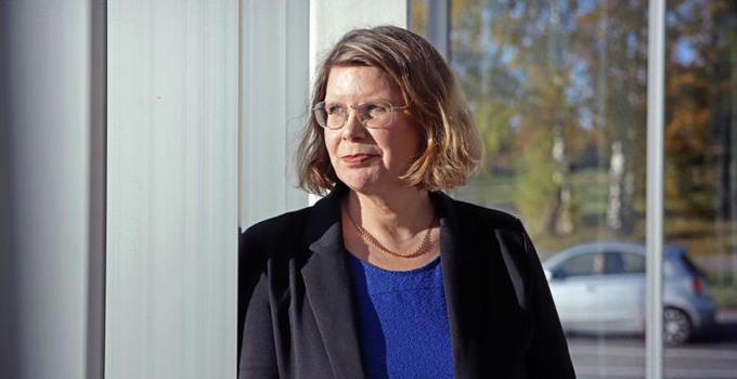 Campus totalförsvars föreståndare Arita Holmberg står vid fönster som speglar träd och bil i bakgrunden